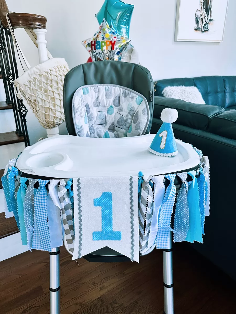 blue decorated high chair with one banner and a first birthday party hat