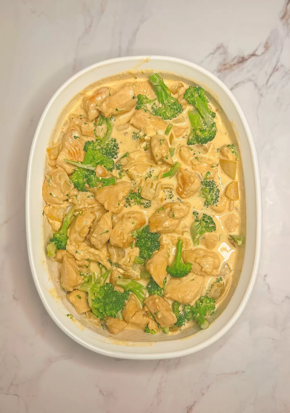 chicken and alfredo sauce with broccoli in a white casserole dish