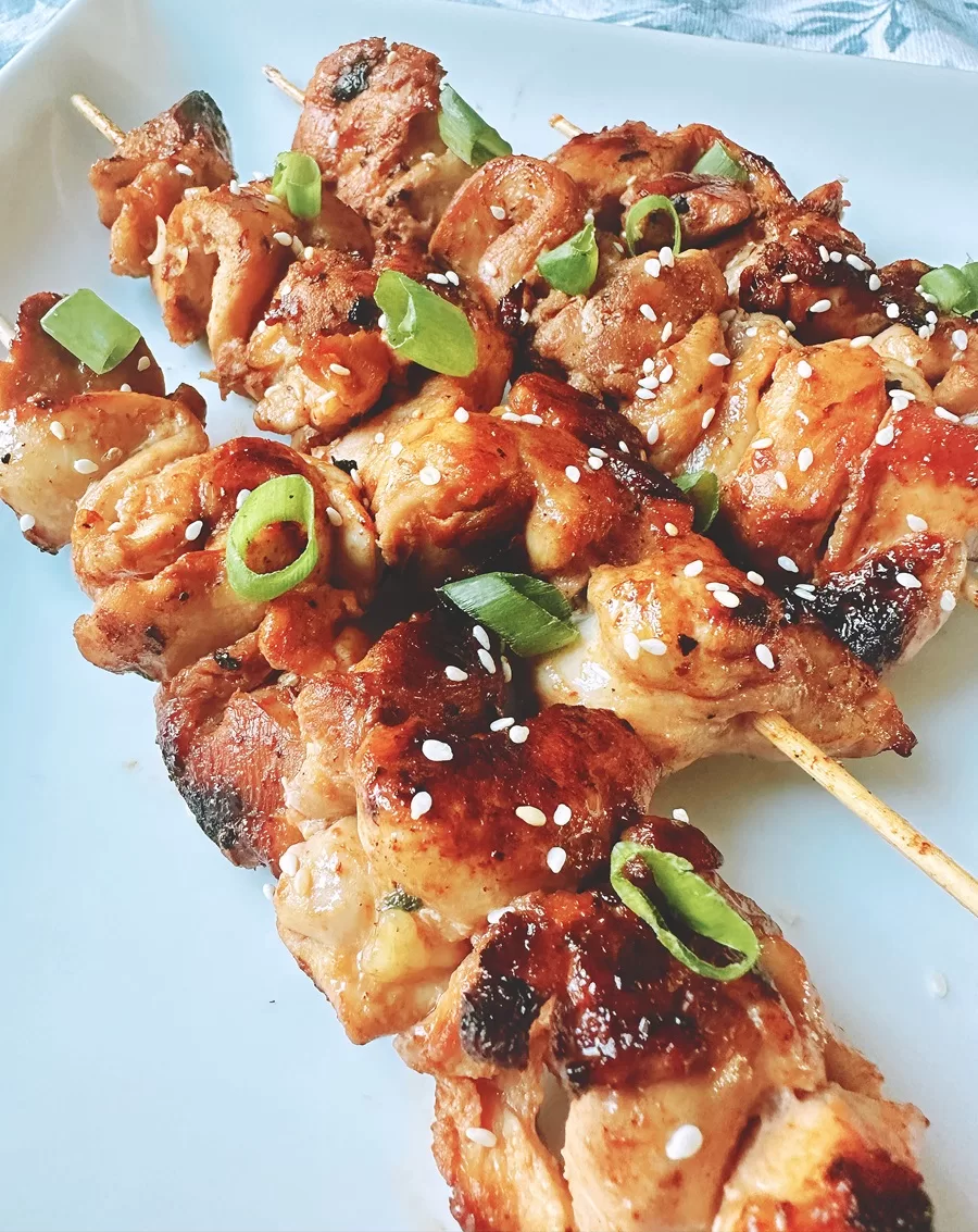 chinese chicken on bamboo skewers topped with sesame seeds and green onion