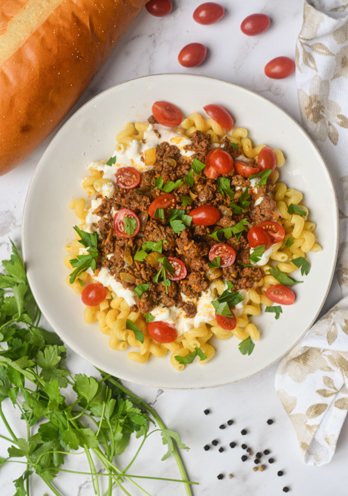 turkish pasta on a white plate surrounded by fresh herbs and bread