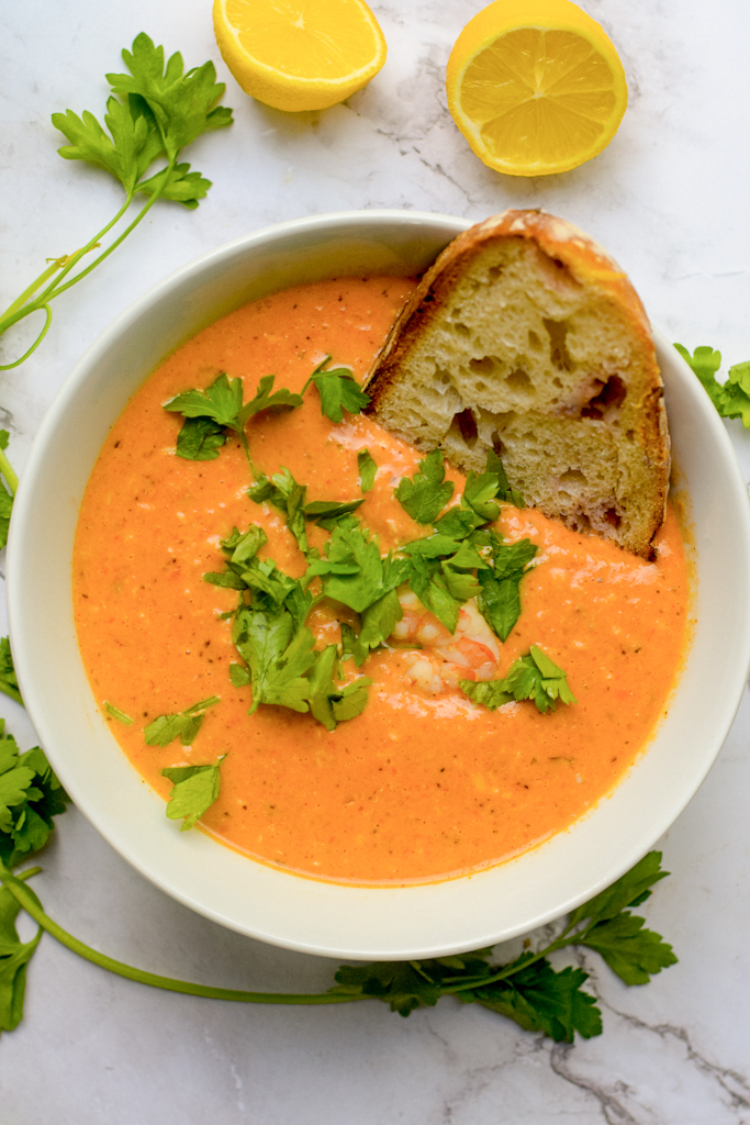 closeup of crab and shrimp seafood bisque in a bowl with lemons and fresh parsley