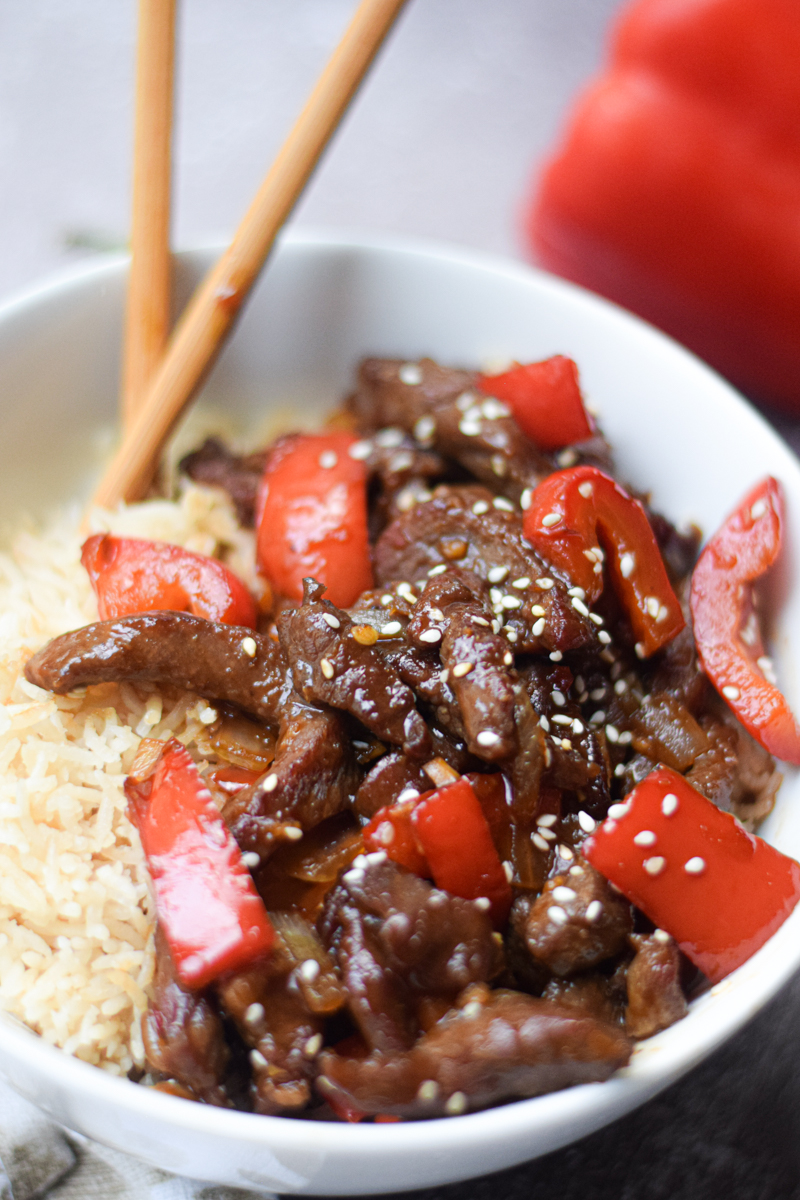 closeup of beijing beef in a bowl with rice and chop sticks