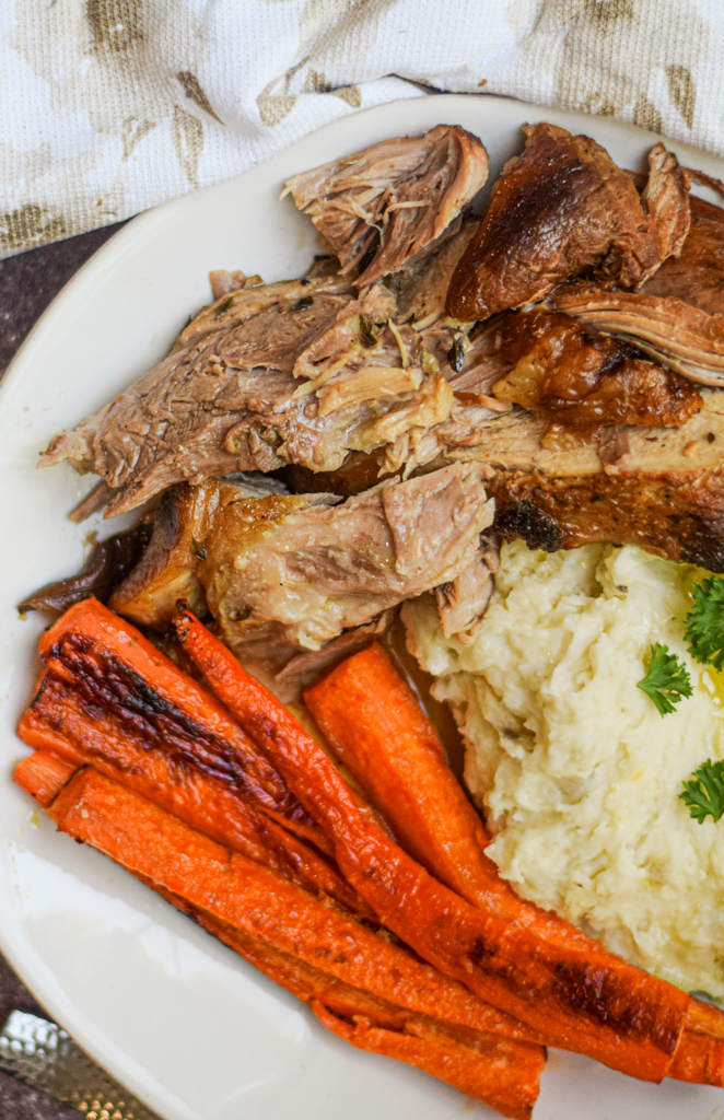 closeup of apple cider braised pork shoulder roast on a plate with carrots and mashed potatoes