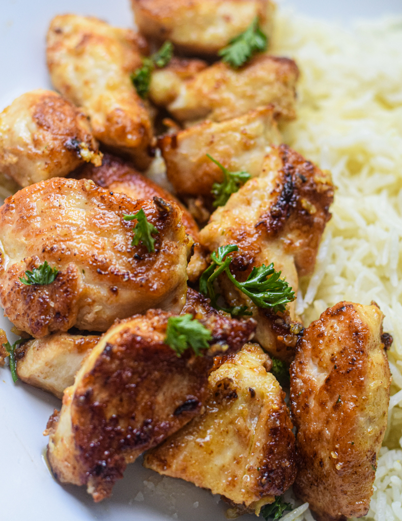 Garlic Butter Chicken Bites on a plate with white rice topped with fresh parsley