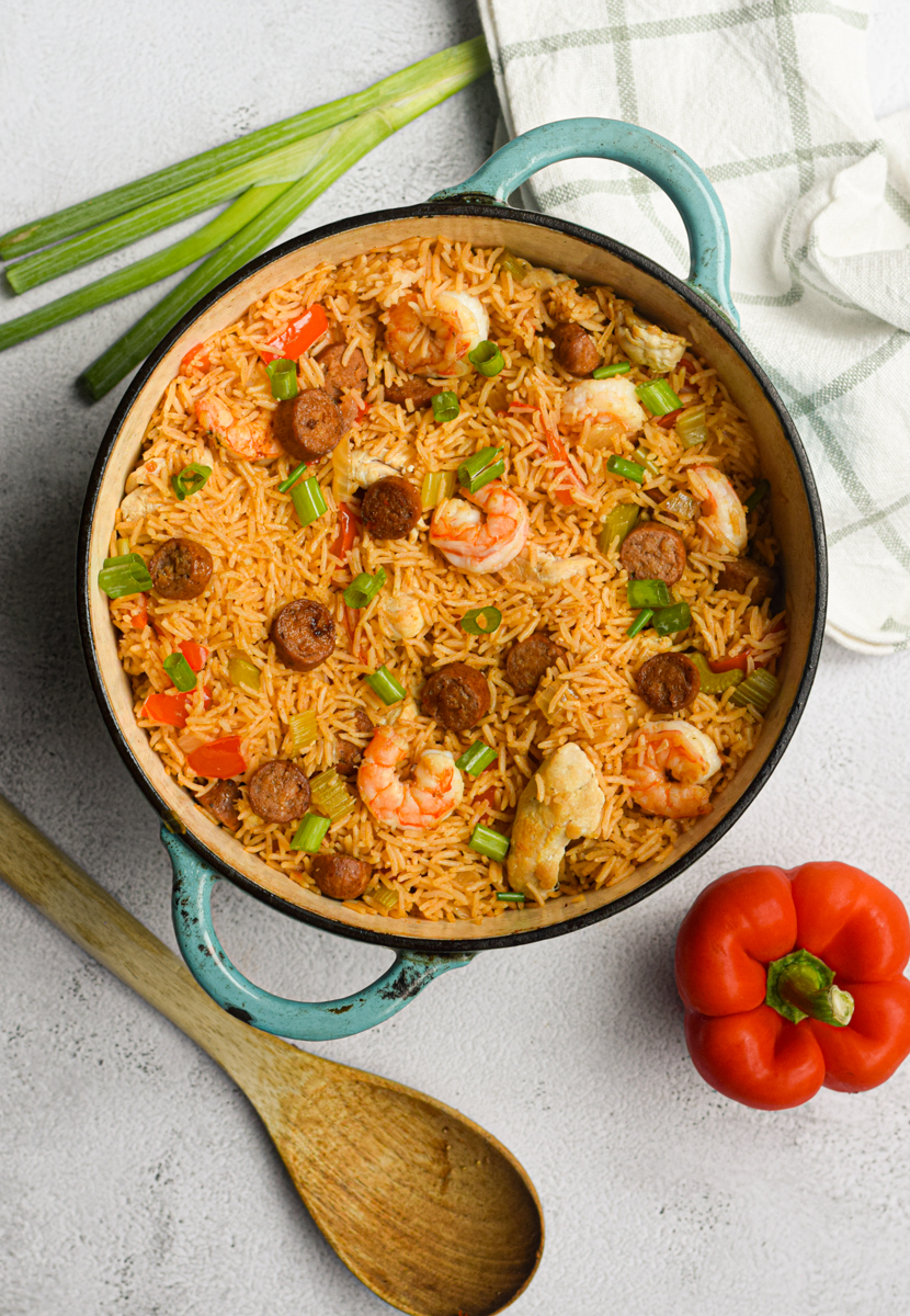 cajun jambalaya in a blue dutch oven surrounded by vegetables