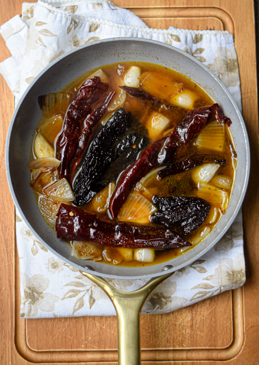 chile peppers and onions cooking in a white frying pan