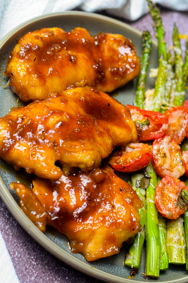 honey garlic chicken on a plate with roasted asparagus and tomato
