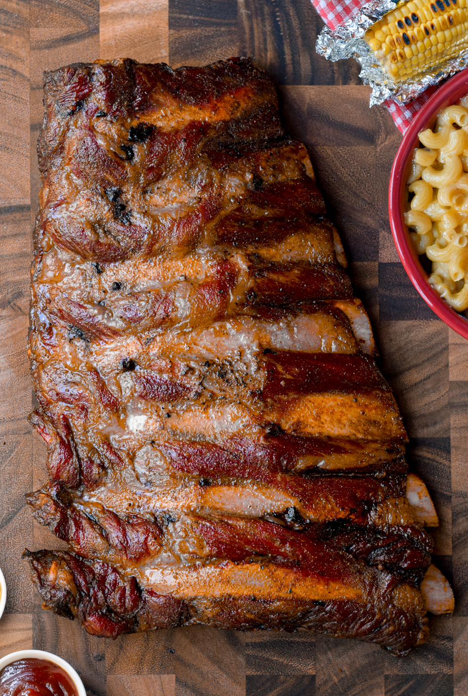 smoked beef back ribs on a wooden cutting board surrounded by side dishes