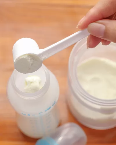 womans hand putting formula into bottle