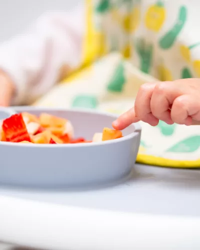 Macro Close up of Baby Hand with a Piece of Fruits Sitting in Child's Chair Kid Eating Healthy Food