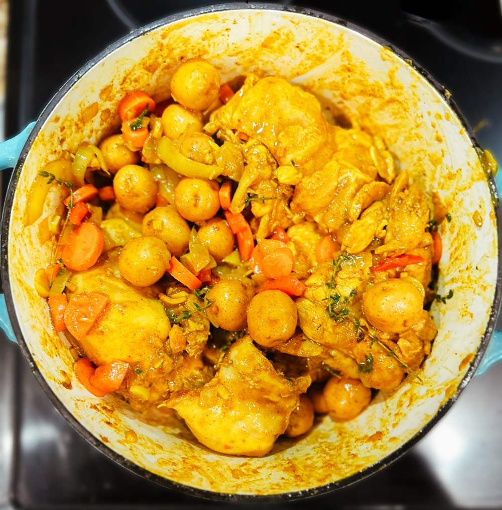 jamaican curry chicken cooking in a dutch oven with wooden spoon