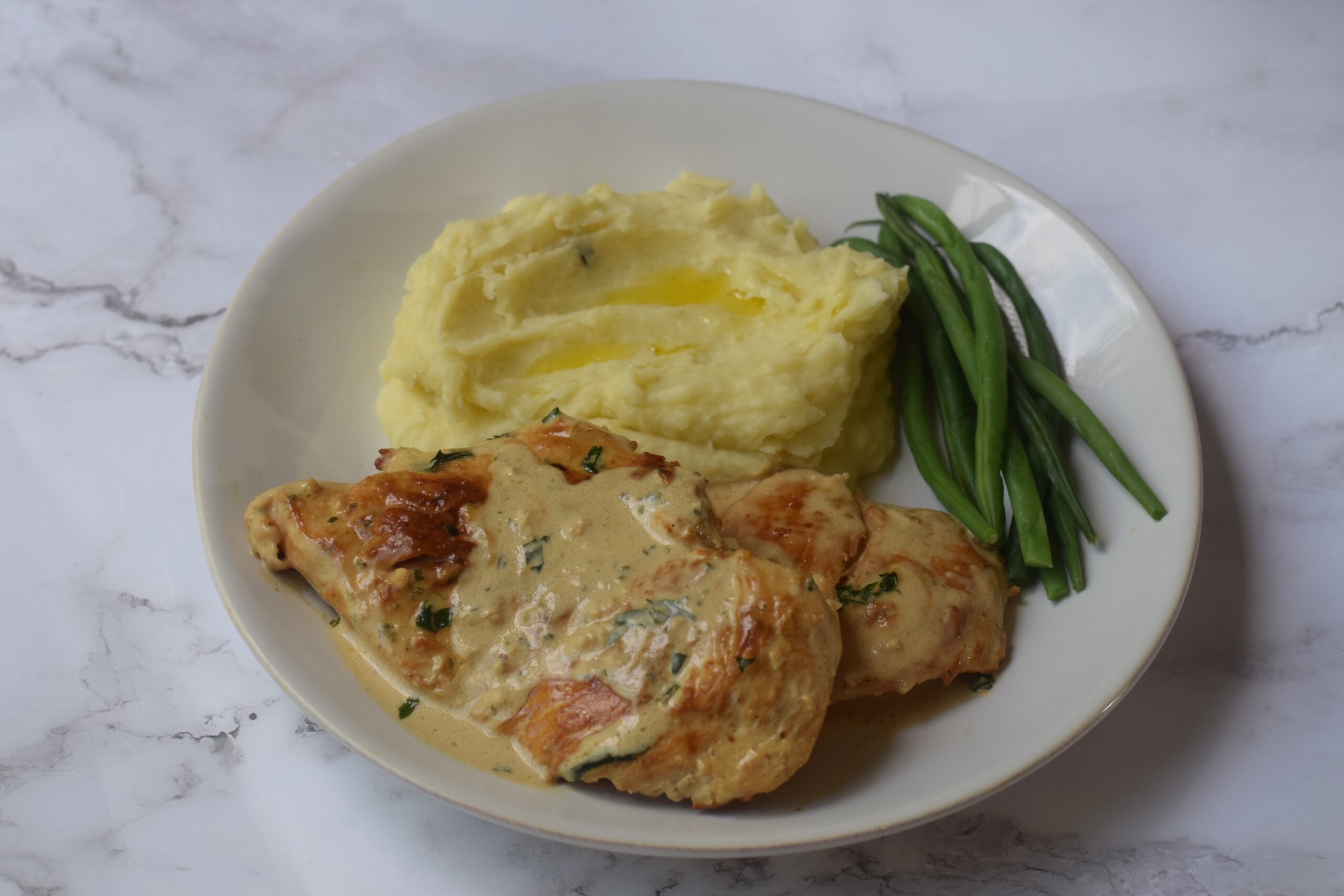 Boursin chicken on a white plate with mashed potatoes and green beans