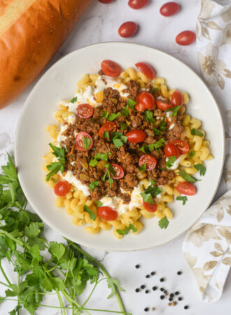 turkish pasta on a white plate surrounded by fresh herbs and bread