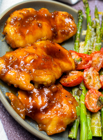 honey garlic chicken on a plate with roasted asparagus and tomato