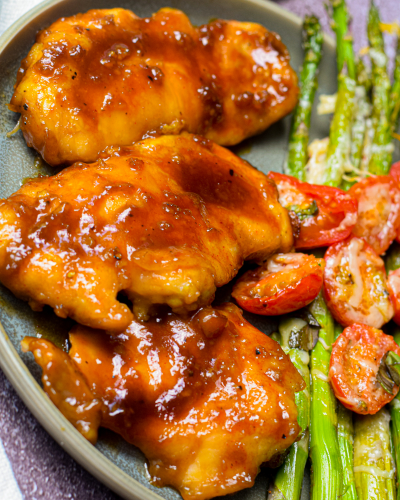 honey garlic chicken on a plate with roasted asparagus and tomato