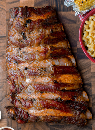 smoked beef back ribs on a wooden cutting board surrounded by side dishes
