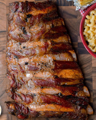 smoked beef back ribs on a wooden cutting board surrounded by side dishes